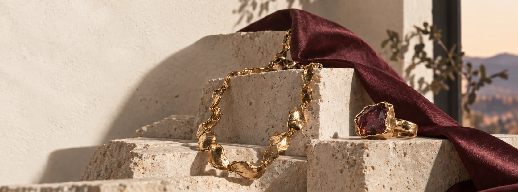 Gold necklace and garnet ring arranged on carved stone with burgundy silk
